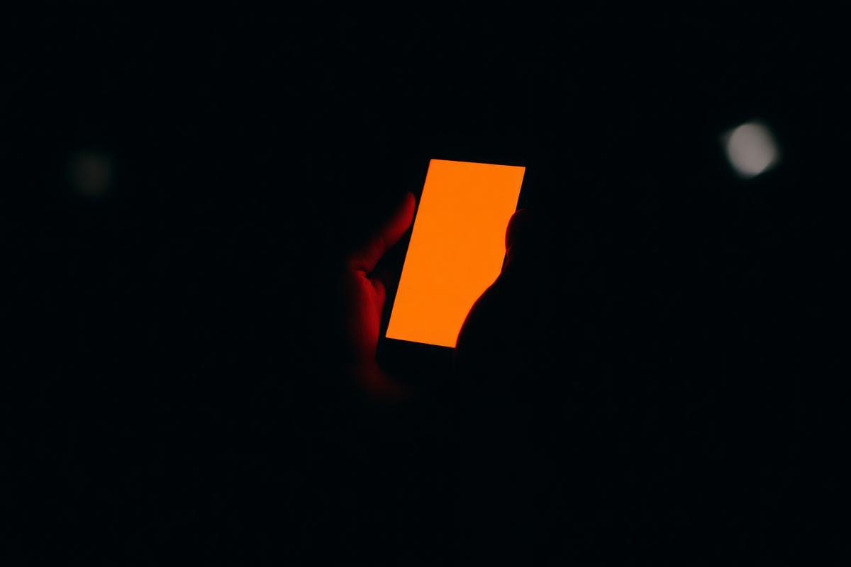 Hand holding a phone glowing orange in a dark room
